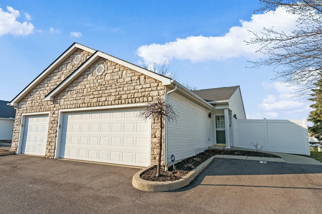 view of property exterior featuring fence, a garage, and driveway