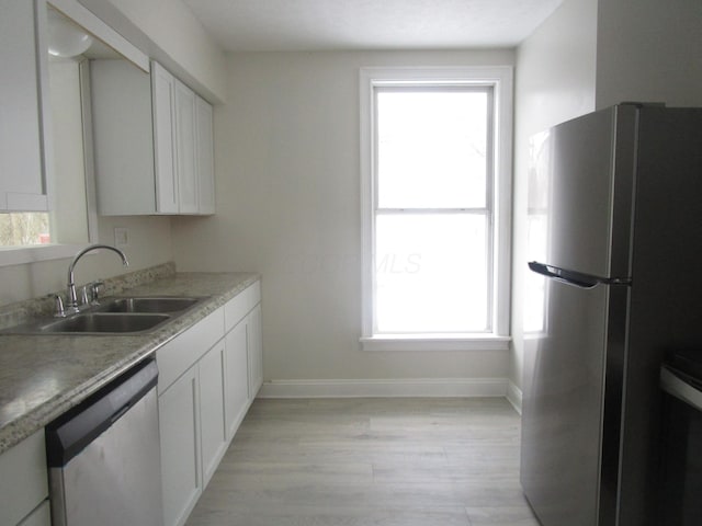 kitchen with light wood-style flooring, a sink, white cabinetry, stainless steel appliances, and baseboards