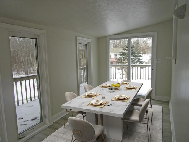 dining room with vaulted ceiling, light wood-style flooring, baseboards, and a textured ceiling