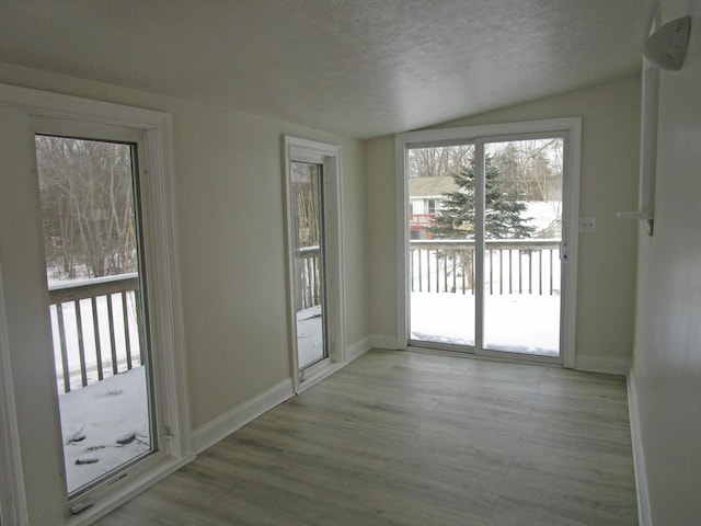 interior space with a textured ceiling, lofted ceiling, baseboards, and wood finished floors