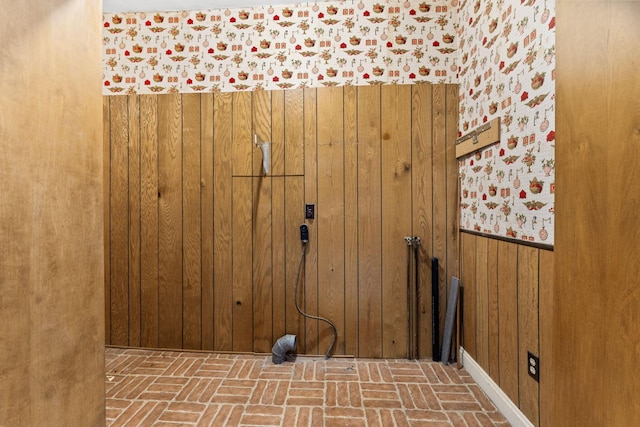 laundry room with wood walls and brick floor