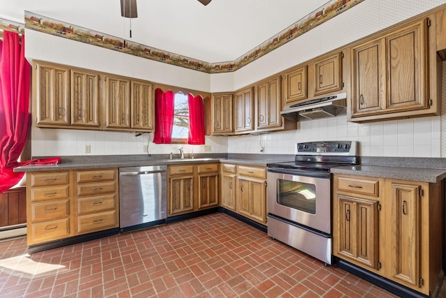 kitchen with dark countertops, backsplash, under cabinet range hood, appliances with stainless steel finishes, and brick floor