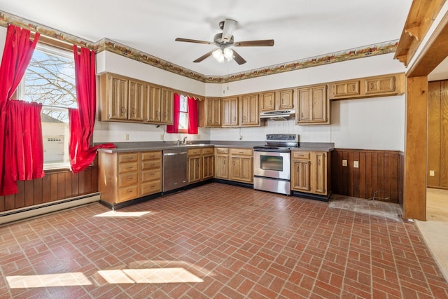 kitchen featuring under cabinet range hood, dark countertops, stainless steel appliances, brick floor, and baseboard heating