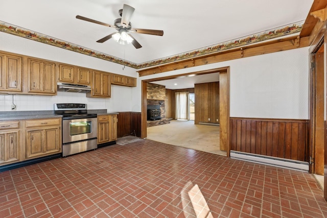 kitchen featuring under cabinet range hood, wainscoting, stainless steel range with electric cooktop, brick floor, and a baseboard radiator