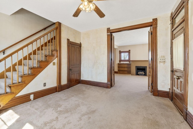 interior space featuring stairway, baseboards, a brick fireplace, and ceiling fan