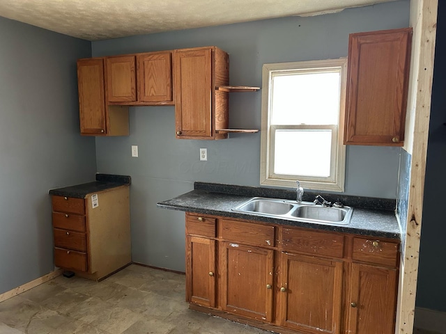 kitchen with open shelves, dark countertops, brown cabinetry, and a sink