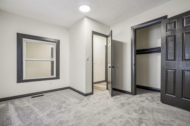 unfurnished bedroom with visible vents, a textured ceiling, a closet, carpet floors, and baseboards