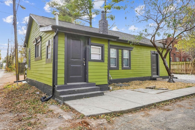 exterior space with a shingled roof, entry steps, a chimney, and fence