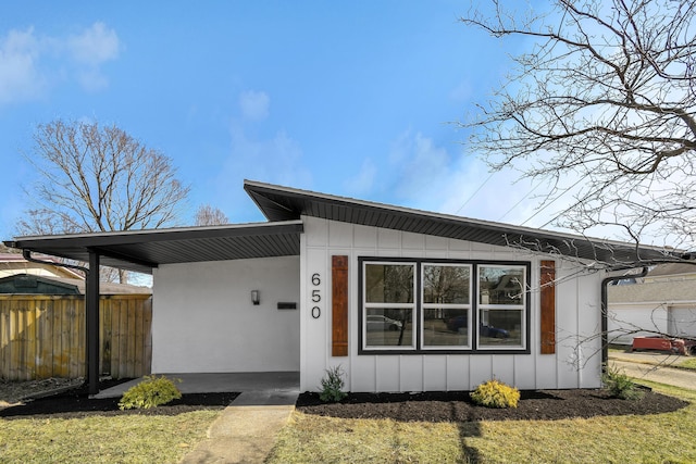 view of front of house featuring an attached carport, fence, board and batten siding, and stucco siding