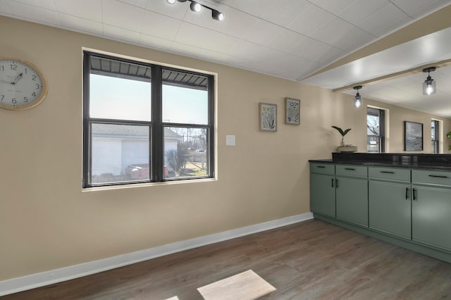 interior space featuring lofted ceiling, dark countertops, green cabinets, baseboards, and dark wood-style flooring