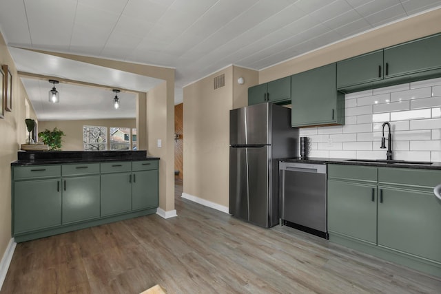 kitchen featuring green cabinetry, light wood-style flooring, a sink, appliances with stainless steel finishes, and dark countertops