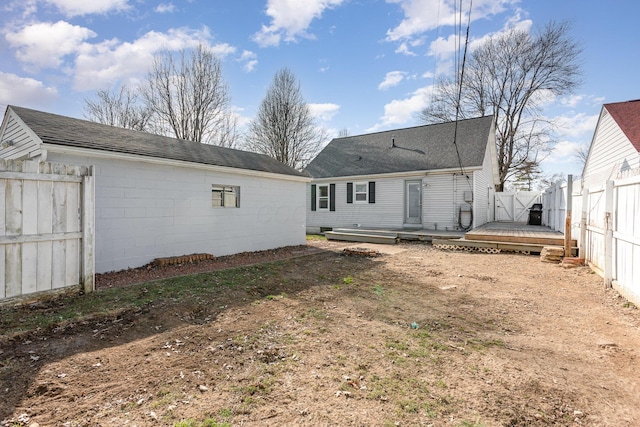 rear view of property with a wooden deck, concrete block siding, fence private yard, and a shingled roof