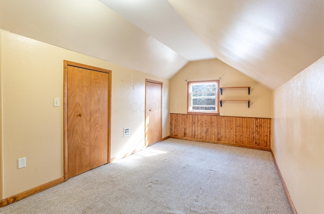 bonus room featuring a wainscoted wall, visible vents, carpet, wooden walls, and lofted ceiling