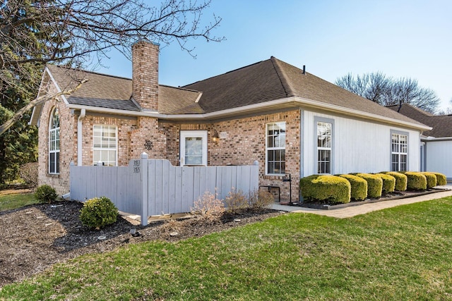 exterior space with a shingled roof, a chimney, a front lawn, a fenced front yard, and brick siding