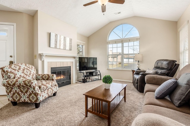 carpeted living room featuring visible vents, vaulted ceiling, a tile fireplace, a textured ceiling, and a ceiling fan