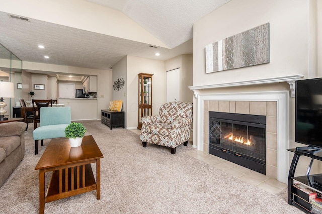 living area featuring visible vents, light carpet, a tiled fireplace, a textured ceiling, and lofted ceiling