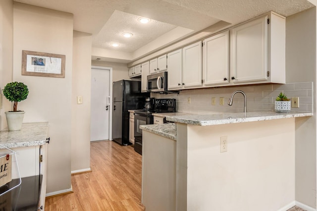 kitchen with black appliances, a textured ceiling, a peninsula, light wood finished floors, and decorative backsplash