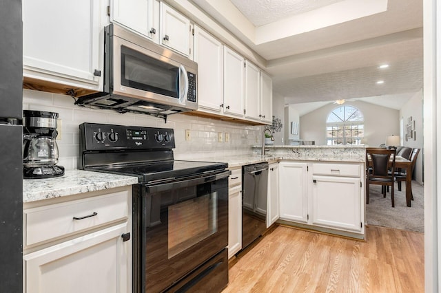 kitchen featuring light wood-type flooring, black appliances, a peninsula, white cabinets, and vaulted ceiling