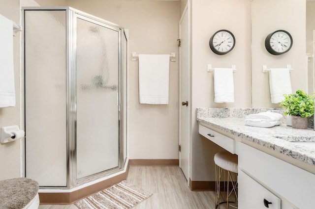 full bathroom with a shower stall, vanity, baseboards, and wood finished floors