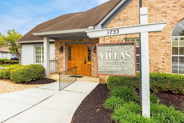 property entrance featuring brick siding and a shingled roof