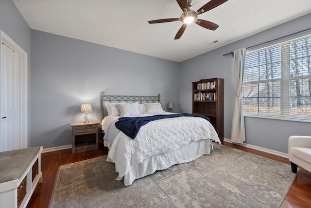 bedroom featuring wood finished floors, visible vents, baseboards, ceiling fan, and a textured ceiling