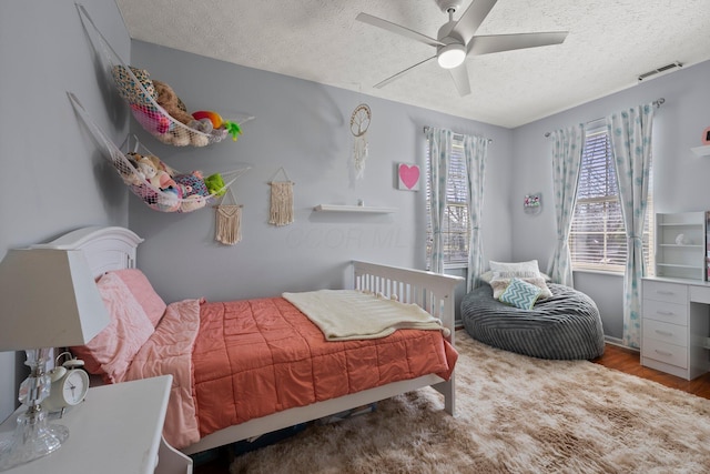 bedroom featuring visible vents, a textured ceiling, ceiling fan, and wood finished floors