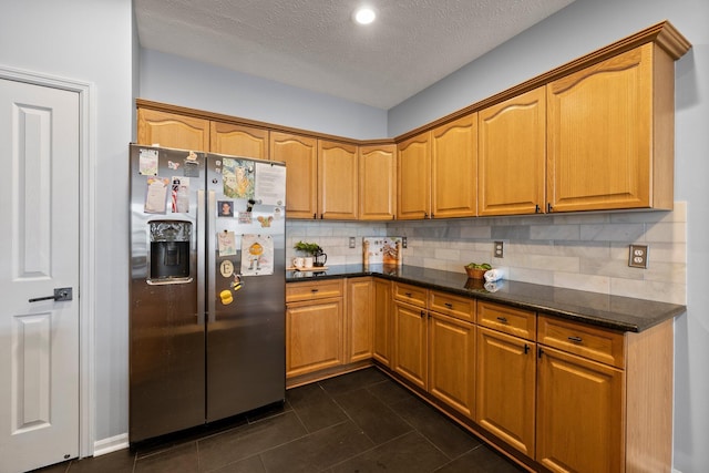 kitchen featuring dark tile patterned flooring, a textured ceiling, dark stone counters, stainless steel fridge, and decorative backsplash