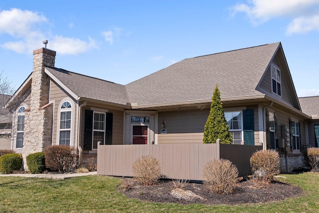 exterior space featuring a front yard, a shingled roof, a chimney, and fence