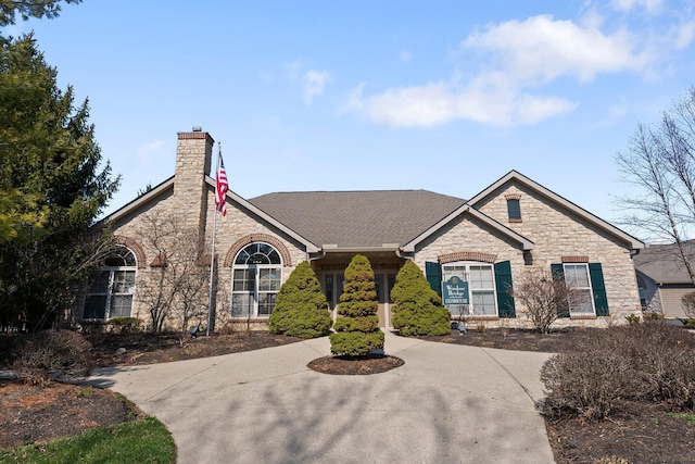 view of front of property with stone siding, roof with shingles, and a chimney