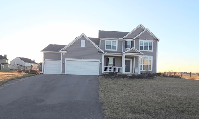 view of front of home featuring a porch, a garage, driveway, and a front yard