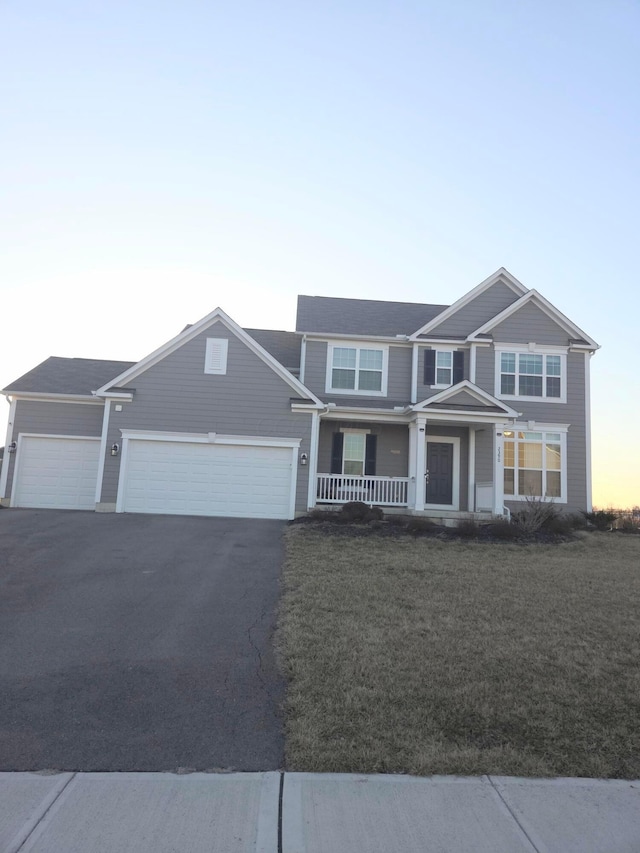 view of front of property featuring driveway, a front yard, covered porch, and an attached garage