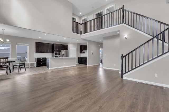 unfurnished living room featuring baseboards, stairs, recessed lighting, light wood-style floors, and a notable chandelier