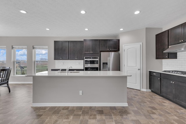 kitchen with light countertops, baseboards, stainless steel appliances, under cabinet range hood, and a sink