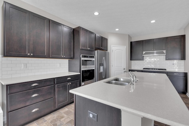 kitchen featuring an island with sink, light countertops, dark brown cabinetry, a sink, and appliances with stainless steel finishes