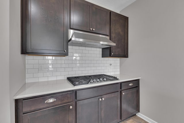 kitchen featuring stainless steel gas cooktop, dark brown cabinetry, under cabinet range hood, and backsplash