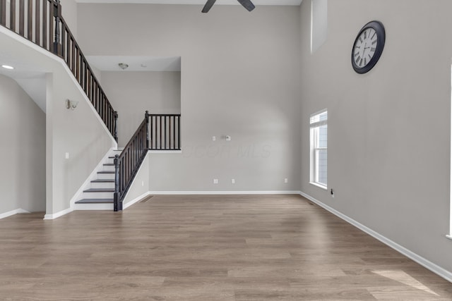 unfurnished living room featuring a high ceiling, baseboards, ceiling fan, and wood finished floors