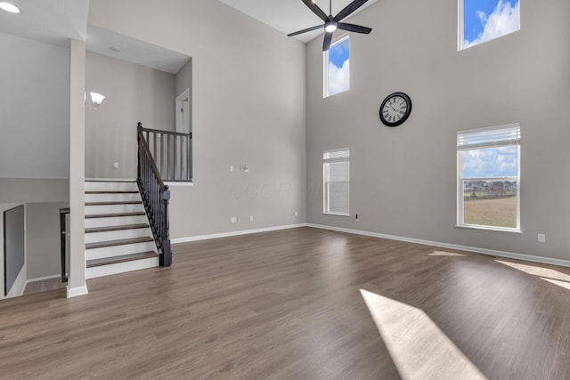 unfurnished living room featuring stairway, a ceiling fan, wood finished floors, baseboards, and a towering ceiling