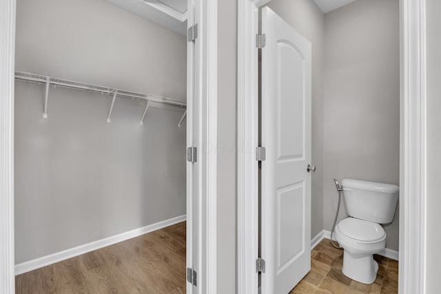 bathroom featuring baseboards, wood finished floors, toilet, and a walk in closet