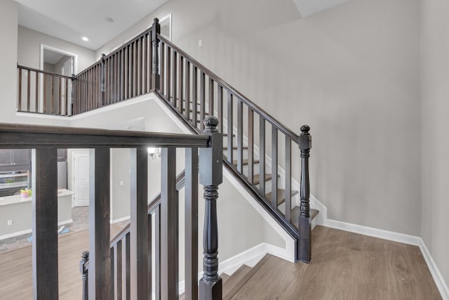 stairway featuring recessed lighting, a towering ceiling, baseboards, and wood finished floors