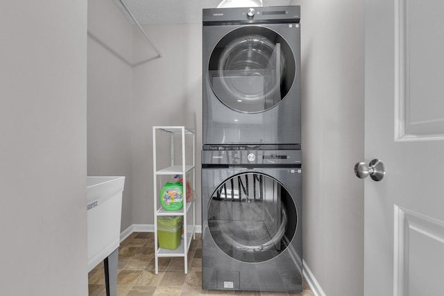 clothes washing area featuring stacked washer / dryer, baseboards, and laundry area