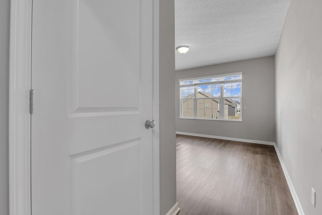 corridor with baseboards, a textured ceiling, and wood finished floors