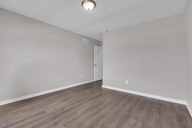 empty room featuring baseboards, visible vents, dark wood-type flooring, and a textured ceiling
