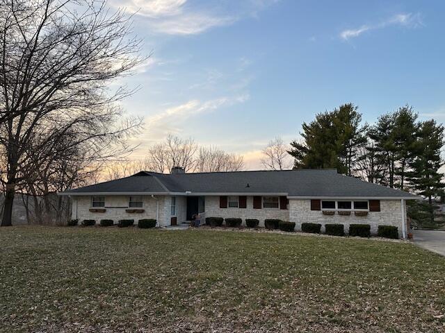 single story home featuring stone siding, a chimney, and a front lawn