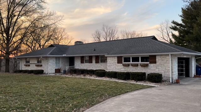 ranch-style house featuring a lawn, stone siding, concrete driveway, an attached garage, and a chimney