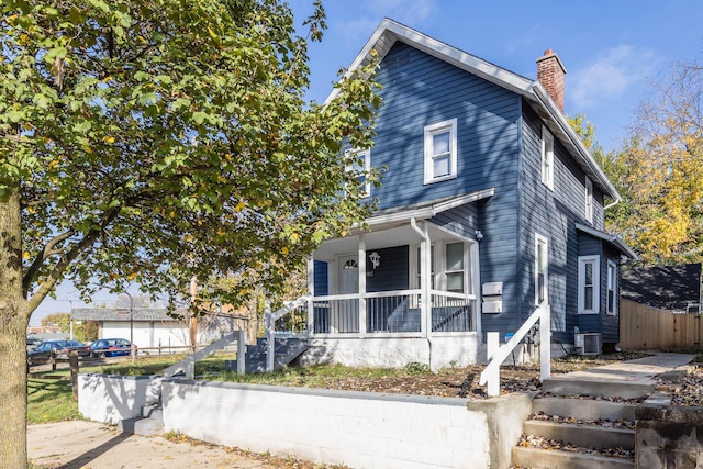 view of front facade featuring covered porch, central air condition unit, fence, and a chimney