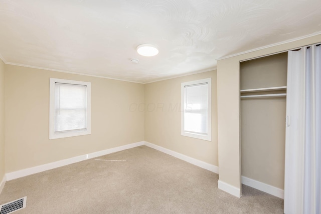 unfurnished bedroom with crown molding, a closet, light carpet, baseboards, and visible vents