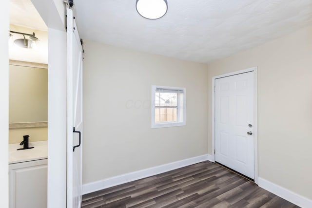 unfurnished room featuring baseboards, a barn door, a sink, and dark wood-style flooring