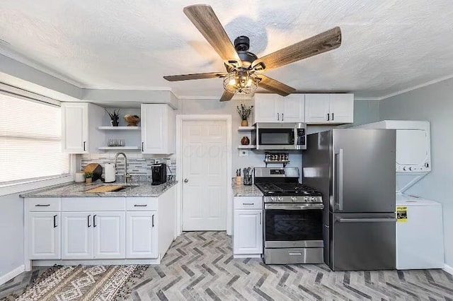 kitchen featuring white cabinetry, open shelves, stacked washer / drying machine, stainless steel appliances, and a sink
