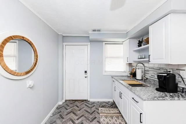 kitchen featuring white cabinetry, baseboards, decorative backsplash, a sink, and visible vents