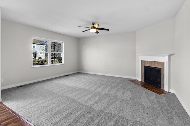 unfurnished living room with visible vents, a ceiling fan, a tiled fireplace, carpet, and baseboards